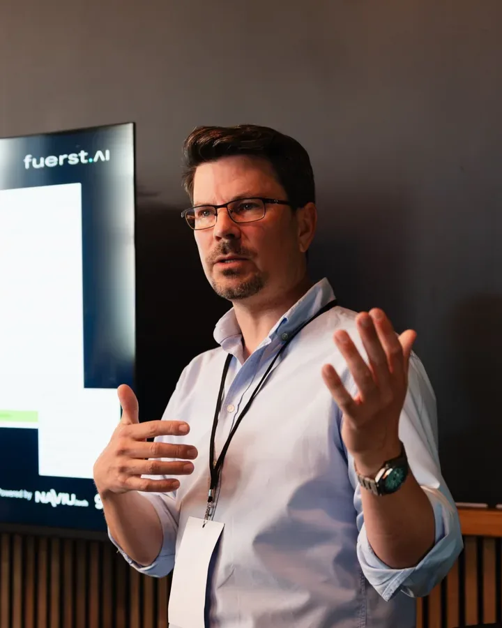 Florian Fürst explaining with open hands in front of the fuerst.ai logo at Berlin AI Day 2026